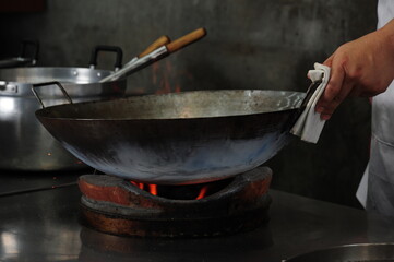 Chef cooking with a wok in fire on charcoal in a kitchen (Asian food, Thai Chinese culinary)