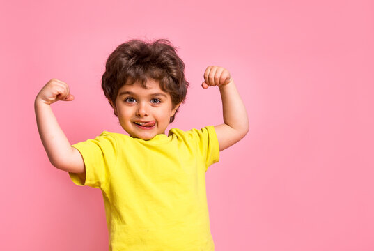 Portrait of little kid boy isolated over pink background showing tongue. Funny little power super hero kid showing muscles. Strength, confidence or defense from bullying. Kindergarten or school kid.