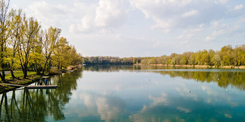 Two unidentifiable people with mask and mobile covering faces, standing Lake for canoeing around Danube river in autumn spring colors with blue sky above and reflection in the lake, Zemnik, Slovakia