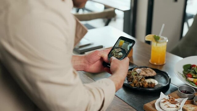Close-up of male hands with smartphone taking pictures of dishes on table
