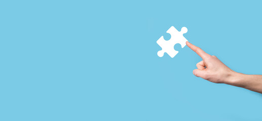 Male hand holding puzzle icon on blue background. pieces representing the merging of two companies or joint venture, partnership, Mergers and acquisition concept.