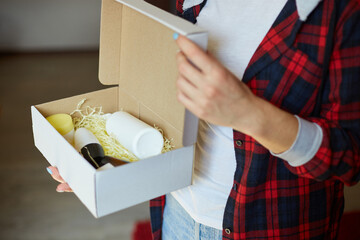 Brunette woman opening, hold in hand online order parcel box with cosmetics at home