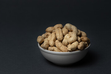 Unpeeled peanuts in bowl on dark background