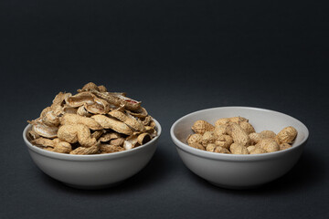 One bowl with peanuts and another one full of peanut shells