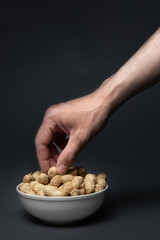Man hand picking unpeeled peanuts from a bowl