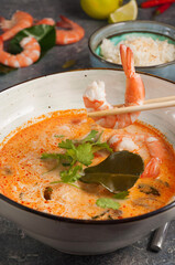 delicious Asian Tom Yam soup. A man holds a shrimp with chopsticks