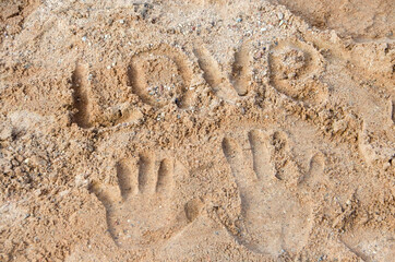 The inscription LOVE and palm prints in the sand