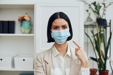 Fototapeta na wymiar young businesswoman in a medical mask pointing at mask in the office