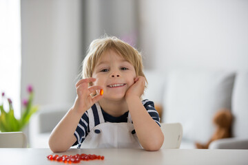 Cute little child, toddler boy, eating alfa omega 3 child supplement vitamin pills at home - obrazy, fototapety, plakaty