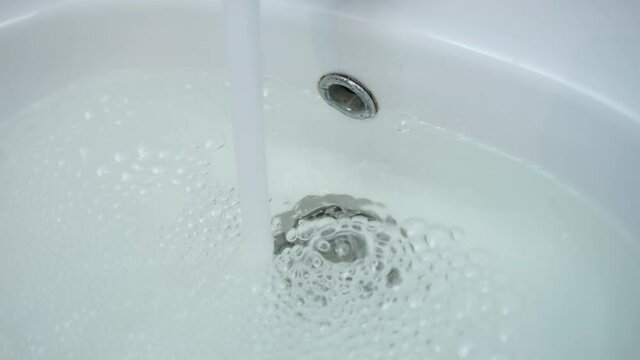 Drain hole in sink is clogged and water is collecting pouring from faucet, closeup view. Clear water pours into broken sink. Bath clogging concept. Sewer is clogged. Danger of flooding the apartment.