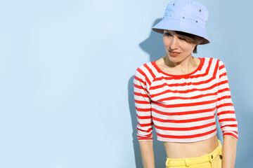 Happy cheerful young woman with short hair, natural makeup over light blue background. Indoor portrait of beautiful brunette young woman wearing blue hat and  bright clothing