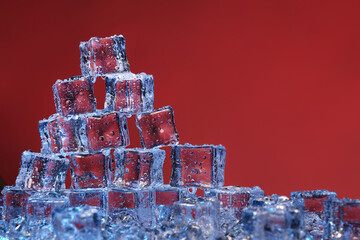 Transparent cold ice cubes on a red background.