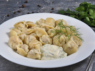 Russian dumplings with meat and garlic sauce on a white plate