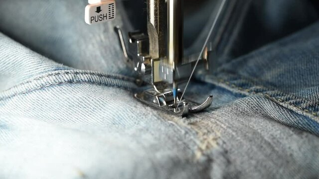 close up of woman sewing for repair blue denim jeans with sewing machine