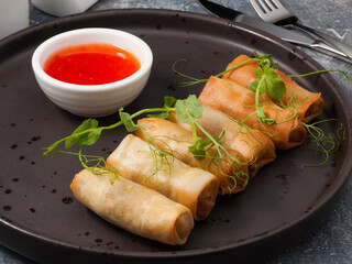 spring rolls with hot sauce and micro greens on a dark plate