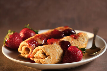 Pancakes with strawberry jam on plate. Pancakes rolls poured berry jam and decorated fresh strawberries.