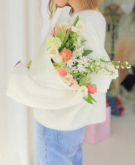 Young woman holding fresh bouquet of beautiful flowers in her hands. Beautiful flower bouquet wrapped in paper.