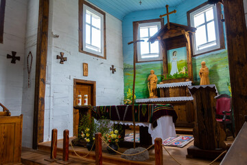 Interior of an old wood church. Blue ceilings, white walls, wooden pews, folk sculptures on the altar. Natural twilight providing soft light.