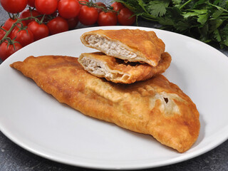 cheburek with chicken on a white plate decorated with vegetables