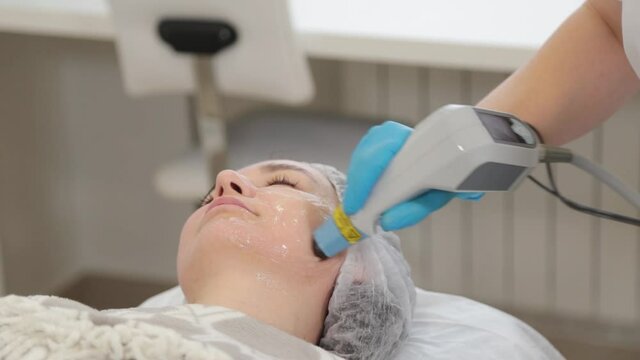 Woman beautician treats her face with a laser. Facial rejuvenation .