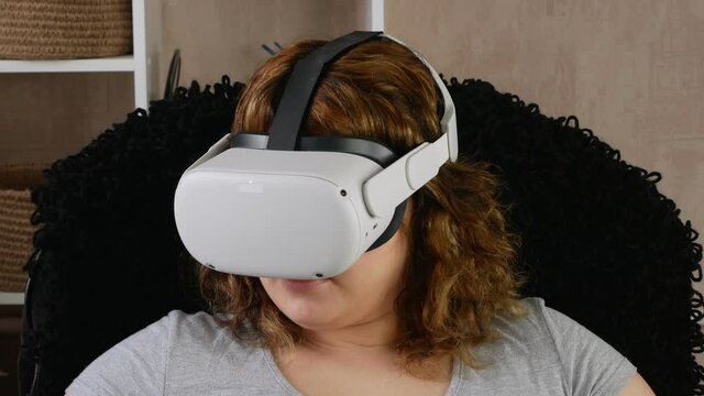 Woman wearing virtual reality glasses. A new generation of computer games. She is surprised and delighted. She likes to watch videos with her helmet on. Leisure in the room.