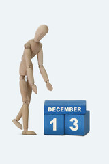 day of the month 13 December calendar . A calendar date on blue cubes and a wooden man standing next to it. White background
