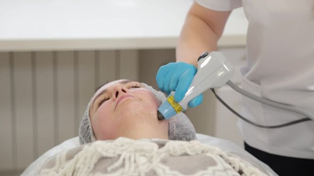 Woman beautician treats her face with a laser. Facial rejuvenation .