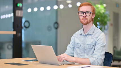 Serious Businessman with Laptop Looking at Camera in Office 