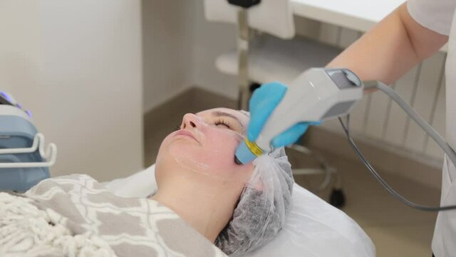 Woman beautician treats her face with a laser. Facial rejuvenation .