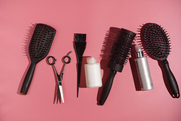 Hair brushes, scissors and tools for hair dresser on pink background in hard light