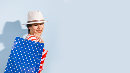 Beautiful woman holding shopping bags stars, stripes in white, blue, red colors  over light  blue...