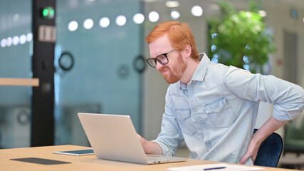 Young Redhead Man with Laptop having Back Pain in Office 