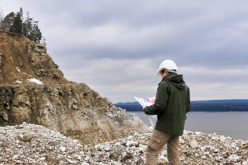 geologist with a map on a steep river bank - obrazy, fototapety, plakaty