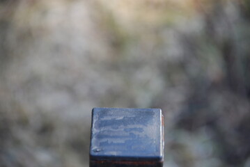 Black metal square on a blurred background. A metal square on a post with faded black paint on a...