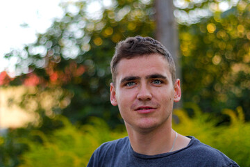 Defocus handsome caucasian young man outdoors portrait. Man surprised, looking in the camera with interest. Blurred nature summer, nature background. Close-up guy 20 years old. Out of focus