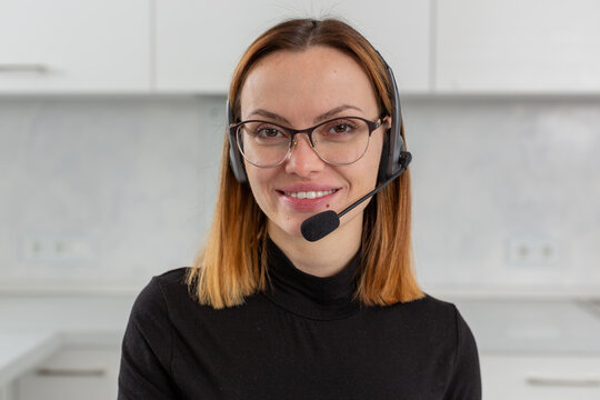 A young happy girl in glasses and a headset smiles and looks directly at the camera. The concept of remote work and learning. High quality photo
