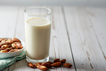 Almond milk in glass with kernel almonds on white wooden background. Healthy eating. Selective focus.