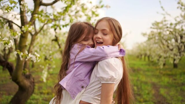 two girls sisters have fun and cuddle in the garden with flowering trees.
