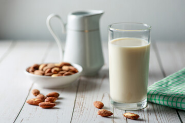 Almond milk in glass with kernel almonds on white wooden background. Healthy eating. Selective focus.