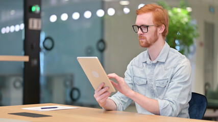 Serious Professional Young Redhead Man using Tablet in Office 