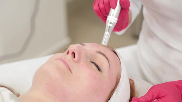 Woman cosmetologist treats her face with a device in the cosmetology office.