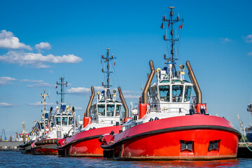 front view of a group of three strong red and white colored tug boats docked in a line in the port...