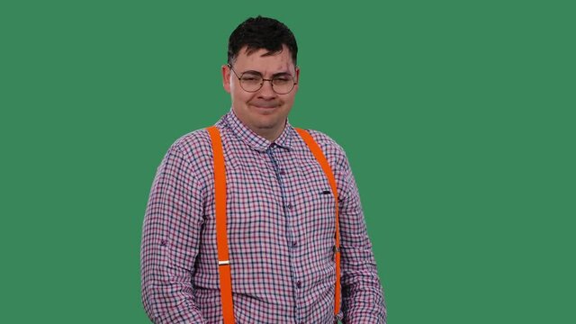 The man raises his eyebrows, flirting, and points his index finger at the camera. Portrait of a man in glasses, in a shirt with orange suspenders in the studio on a green screen. Slow motion. Close up