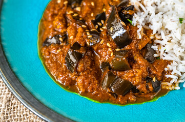 Masala from roasted aubergine in spicy tomato sauce with basmati rice in blue plate