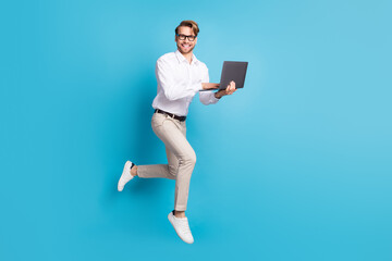 Full length body size view of attractive cheerful man jumping using laptop it expert isolated over bright blue color background