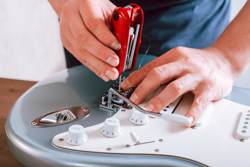 Guitar master adjusting bridge saddle on tremolo of electric guitar using multitool