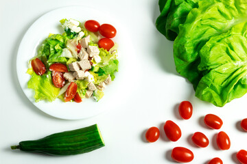 Chicken salad, scattered cherry tomatoes, green cucumber, on a white background, in a close-up, isolated, top view