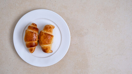 Two classic french croissants on white plate on the table. Top view. Morning routine and Breakfast concept. Light background. Copy space.