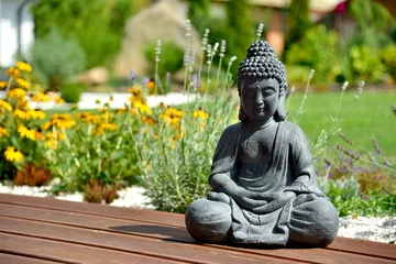 Gartenposter A closeup of a small Buddha statue in a garden with a blurry background © Radek Havlicek
