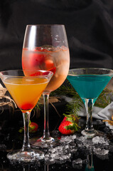 cocktails on a black background decorated with ice and strawberries